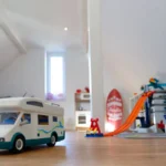 Ein Spielzeugauto steht auf dem Boden, im Hintergrund steht eine Kinder Parkgarage.